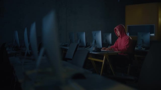 集中的男学生独自坐在大学信息学室，晚上在计算机科学项目上工作。年轻的学者在大学学习计算机，在课堂上编