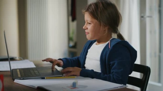 真实的小微笑女孩小学生的镜头正在用笔记本电脑进行视频通话，以便在家里的远程教育期间与虚拟教室中的老师