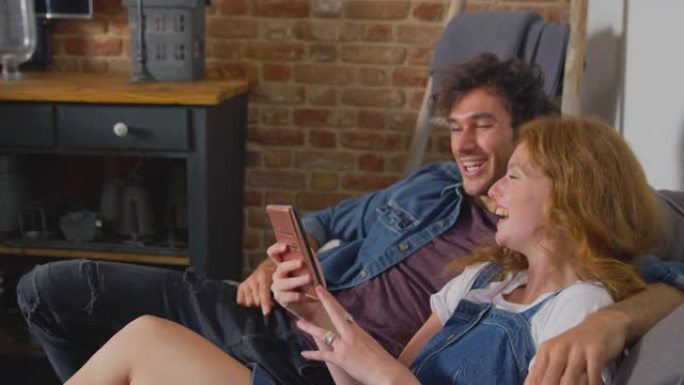 情侣坐在家里休息室的沙发上一起看手机