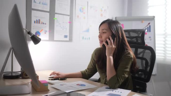 亚洲女商人在电脑上工作，在办公室接电话