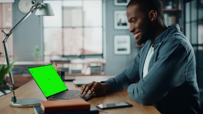 英俊的黑人非洲裔美国专家在家庭客厅的笔记本电脑上工作，绿屏模拟显示。自由职业者在社交网络上通过互联网