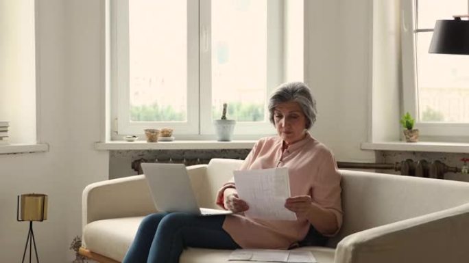 年长的女人坐在笔记本电脑的沙发上，分析论文，看上去很困惑