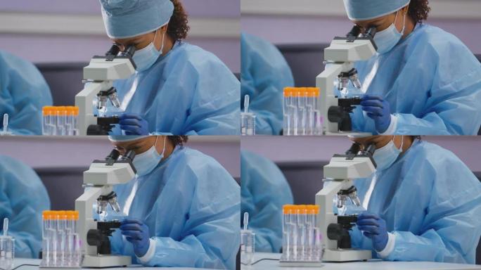 穿着个人防护装备的实验室女工作人员在显微镜下分析载玻片