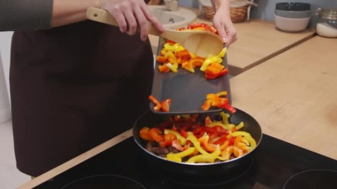 女人在煎锅中的牛肉条上加入甜椒