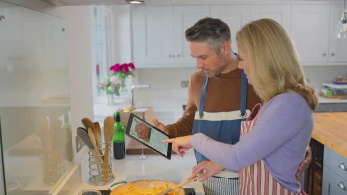 家里的成熟夫妇在一起准备饭菜时，在厨房的数字平板电脑上遵循食谱
