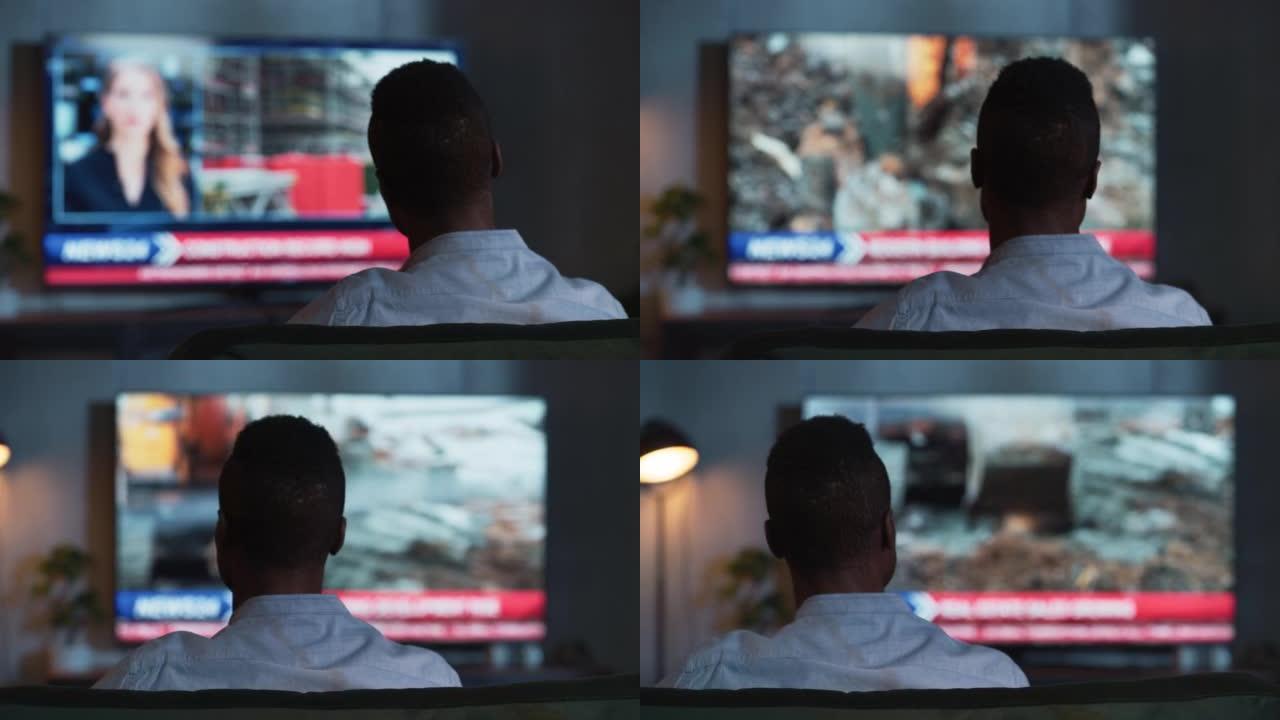 黑人男子晚上坐在沙发上看电视直播新闻的后景。娱乐和技术概念。后视图移动镜头与模糊的电视屏幕