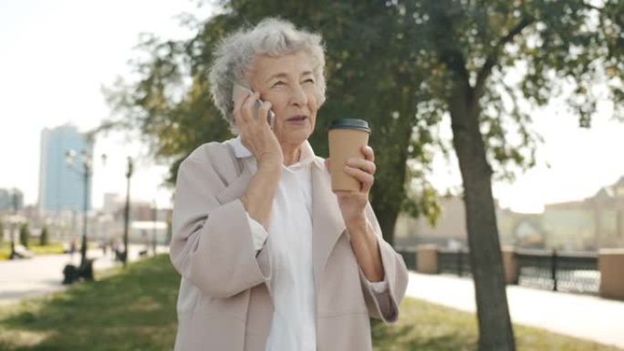 美丽的老太太在手机上聊天，在城市街道上喝酒去户外喝咖啡