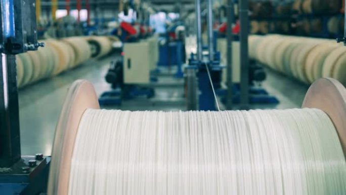 在工厂，白线从大型木制线轴上展开。现代工厂设施中的工业设备。
