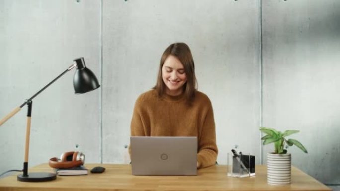 专业创意微笑的女人坐在办公室的办公桌前，在笔记本电脑上工作。现代简约设计办公室: 富有成效的成功女商