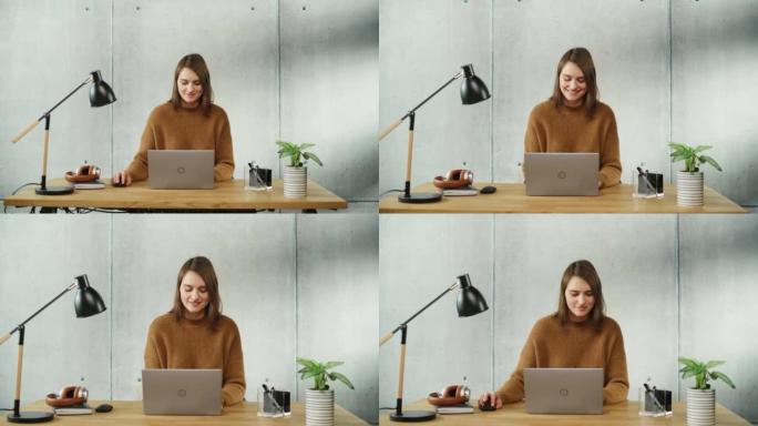 专业创意微笑的女人坐在办公室的办公桌前，在笔记本电脑上工作。现代简约设计办公室: 富有成效的成功女商