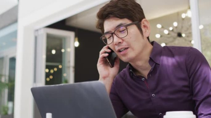 亚洲男子坐在咖啡馆里用智能手机聊天并使用笔记本电脑