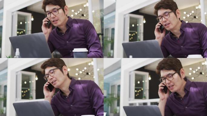 亚洲男子坐在咖啡馆里用智能手机聊天并使用笔记本电脑