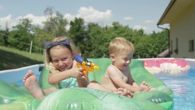 特写: 开朗的哥哥和姐姐漂浮在游泳池里玩水枪