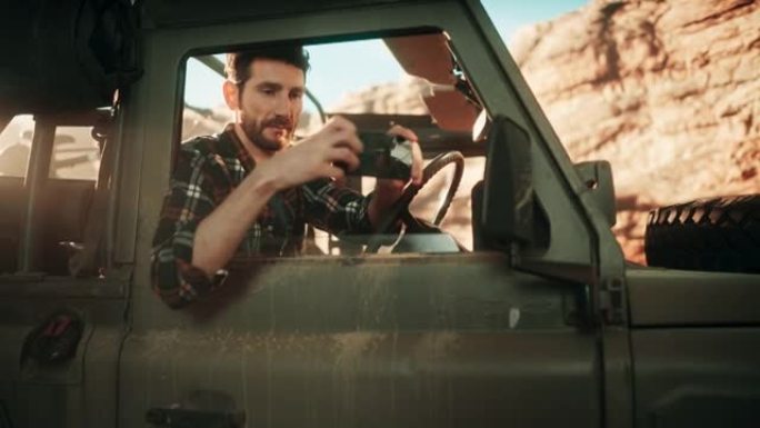 沙漠之旅: 男性探险家的肖像使用智能手机在越野SUV穿越岩石峡谷时拍照。带有奇妙性质的社交媒体帖子的