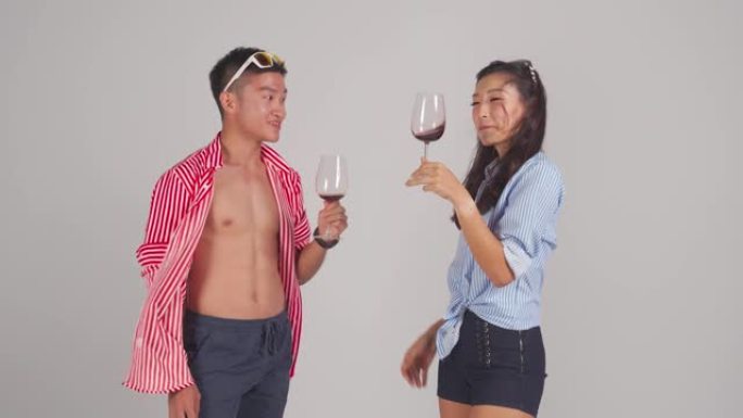 时尚的亚洲中国夫妇手持酒杯跳舞，手持酒杯工作室拍摄，背景为灰色