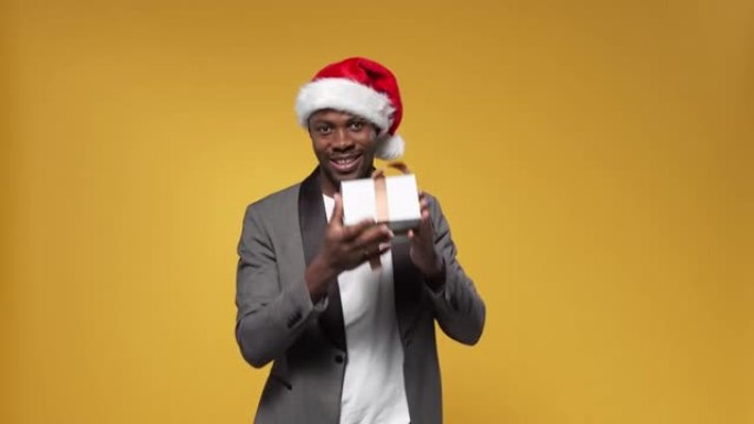 一个戴着圣诞帽的黑皮肤男人抓住一个扔给他的礼品盒，开心地微笑着