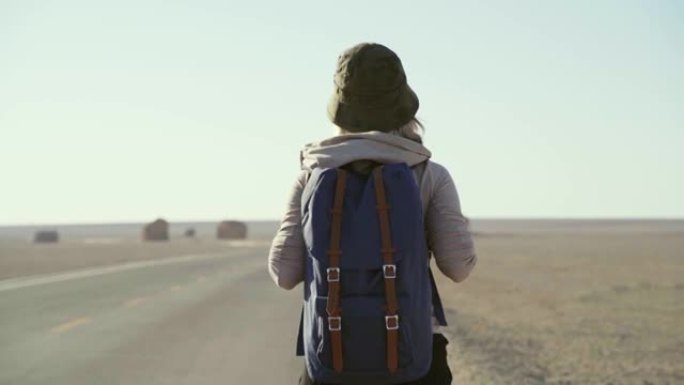 亚洲女性徒步旅行者在沙漠中的高速公路上行走