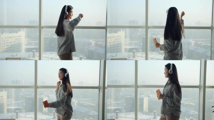 亚洲女人戴着耳机跳舞的慢动作在全景窗户背景下在家玩耍