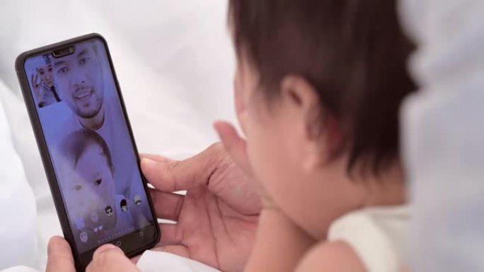 亚洲父亲和新生儿的幸福家庭在10个月的视频会议上打电话给母亲或亲戚，在社交距离期间一起呆在家里，以防