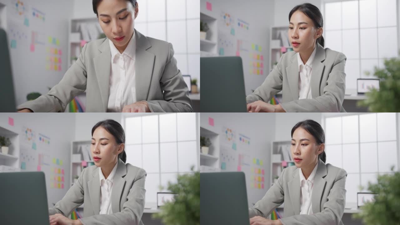年轻的亚洲开朗的职业女商人坐在桌子上，手提电脑在现代办公室工作在线营销。