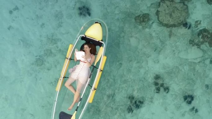 美好的一天的鸟瞰图，25岁的年轻女性躺在海上船上看书。热带度假活动概念。