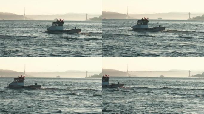 挥舞着土耳其国旗的小型码头船沿着蓝色的夏季海浪，遥远的桥梁背景航行。
