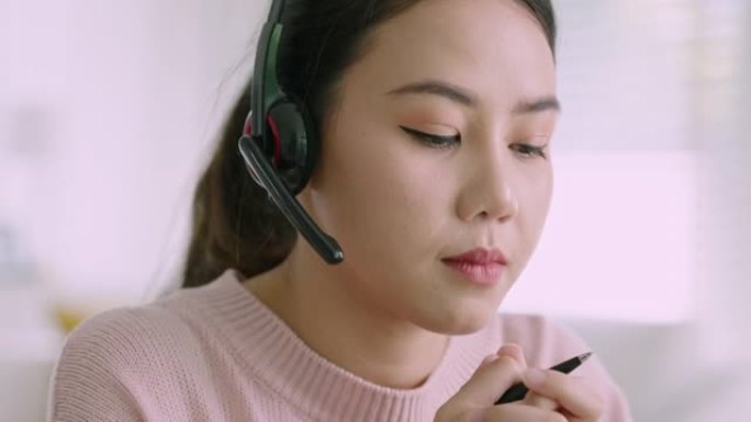 亚洲女性在家戴无线耳机工作视频通话