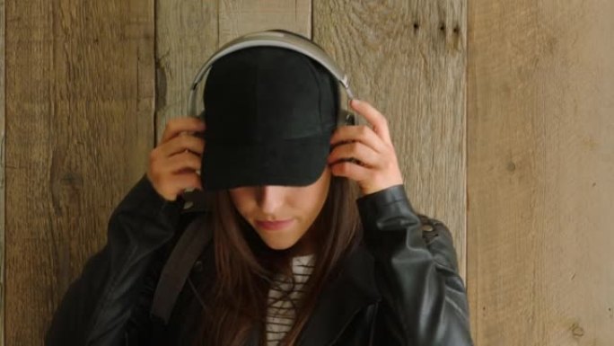 一位很酷的大学生，在木墙上戴着耳机听音乐。一个很酷的年轻女子通过听耳机欣赏音乐