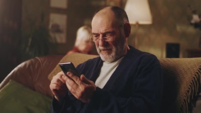 快乐的老人在沙发上使用手机