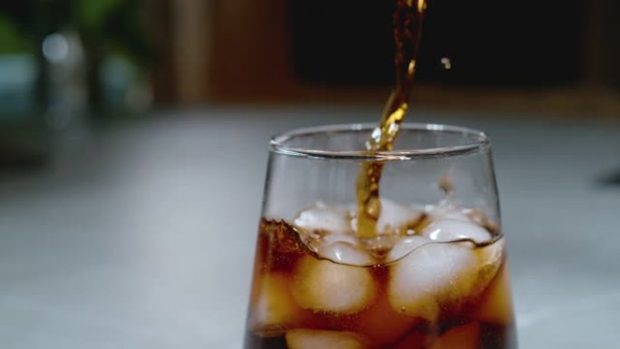 关闭，DOF: 深色碳酸可乐饮料滴入充满融化冰的玻璃杯中。