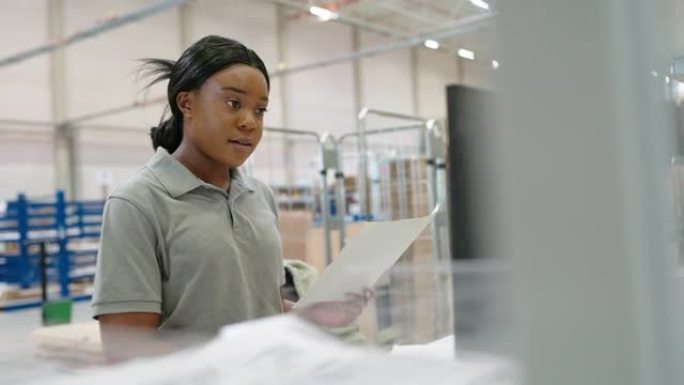 非洲妇女在仓库里用纸在计算机上工作