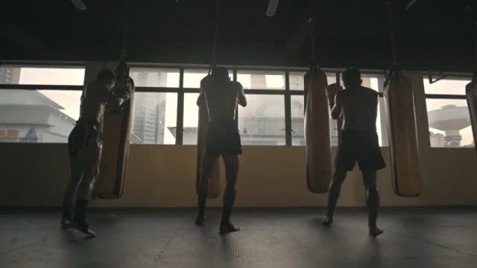 后视图极限运动亚洲男子泰拳拳击沙袋连续在健身俱乐部练习