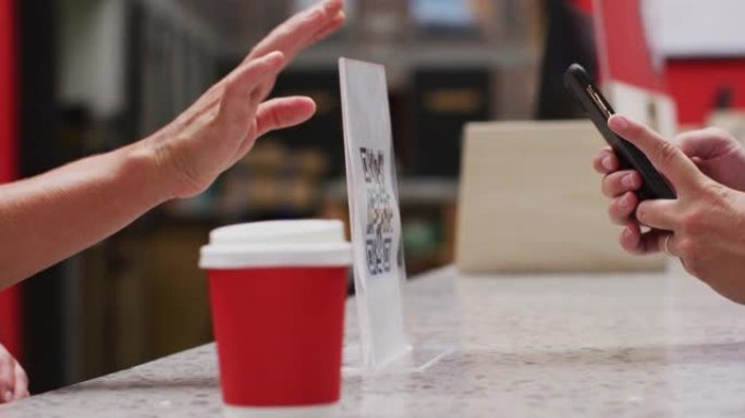 女人的中间部分用智能手机扫描qr码以在咖啡馆付款