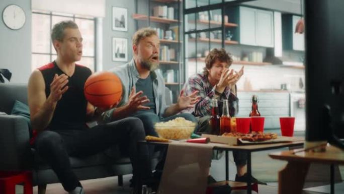 在家里，三个快乐的篮球迷坐在电视上的沙发上观看比赛，庆祝得分和运动队冠军的胜利。当最喜欢的俱乐部玩耍