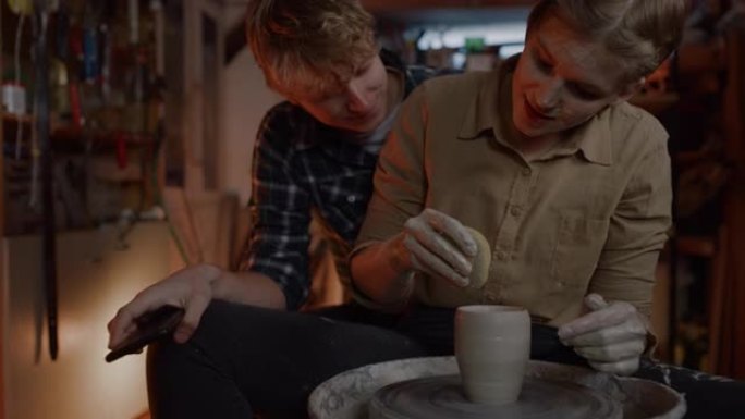 SLO MO年轻夫妇在陶艺工作室中塑粘土时使用智能手机
