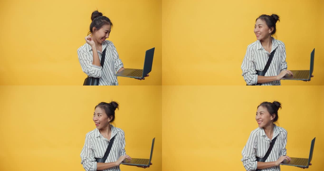快乐美丽亚洲青年休闲女孩打字笔记本电脑站在孤立的黄色空白空间背景微笑给标志展示成功购买在线广告。