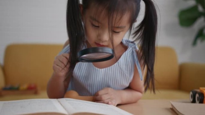 年轻的亚洲女孩读书放大镜在客厅
