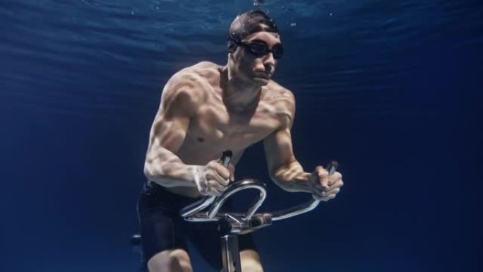 年轻的男性运动员的电影镜头肌肉发达，正在水下固定的骑行机上努力和决心地运动。运动、健身、健康生活方式