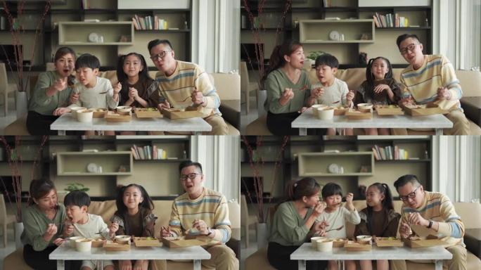 亚洲华人年轻家庭在周末在客厅的电视前享受外卖食物