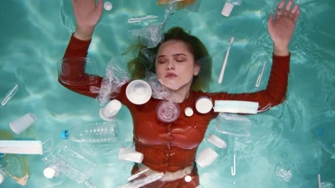 电影的俯视图，美丽的女人躺在水面上，周围有各种塑料包装废料慢动作。