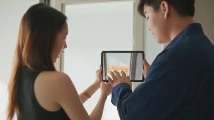 情侣手持数字平板电脑和手机，带增强现实应用程序模拟家庭家具
