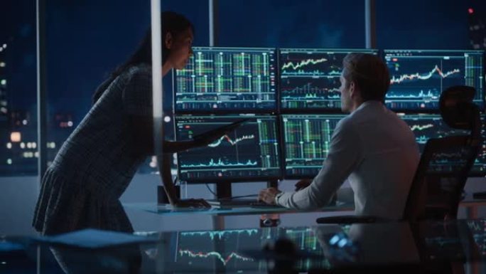 财务分析师晚上在工作中与投资银行家交谈。在多显示器工作站上聊天实时股票图表数据。商人在经纪人代理办公