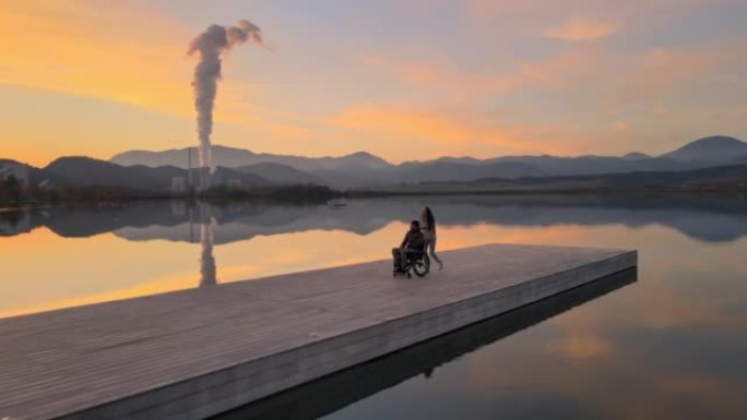 妇女与残疾丈夫坐在轮椅上在码头上行走