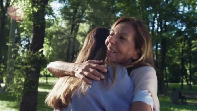 在阳光明媚的日子里，在绿色公园，电影拍摄的快乐孙女给祖母一个情感的拥抱，以示爱和尊重。生活观念，祖父