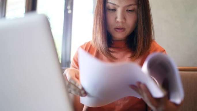 使用笔记本电脑并阅读文档进行分析的亚洲女性