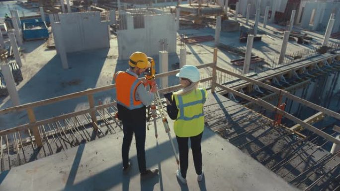 建筑工人使用经纬仪测量光学仪器测量建筑工地上水平和垂直平面的角度。工程师和建筑师在测量师旁边使用平板