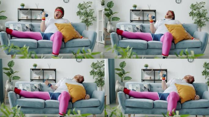 慢动作懒惰的超重男子用哑铃和打哈欠训练然后睡在家里的沙发上