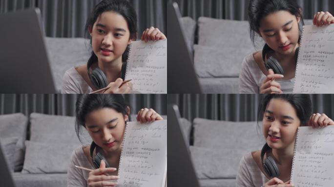 特写镜头迷人的亚洲少女通过笔记本电脑向朋友解释数学作业。她在冠状病毒锁定的同时在家使用在线视频通话教