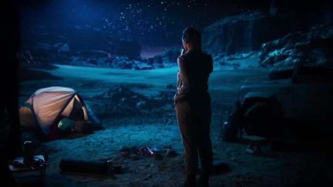 幸福的夫妻在夜晚的峡谷中露营，站在篝火旁，慈爱而浪漫地牵着手看着星空。两个旅行的人在自然鼓舞人心的假