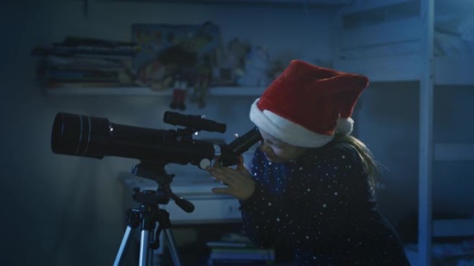 电影之夜拍摄的两个穿着星空睡衣和圣诞老人帽子的快乐小女孩姐妹正在通过望远镜观看圣诞节那天圣诞老人在星